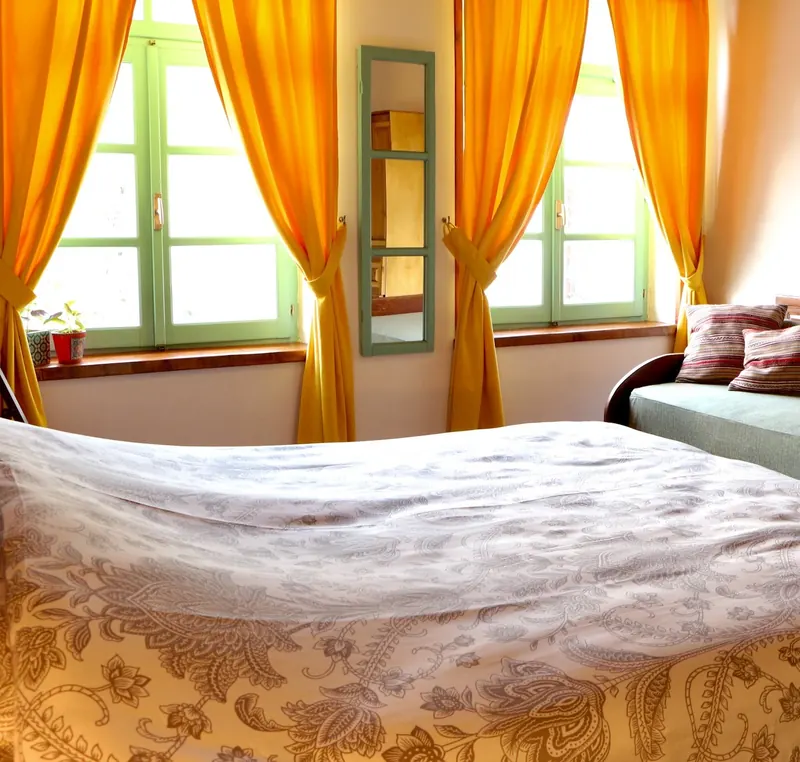 Private room with orange curtains, green window frames and a day bed